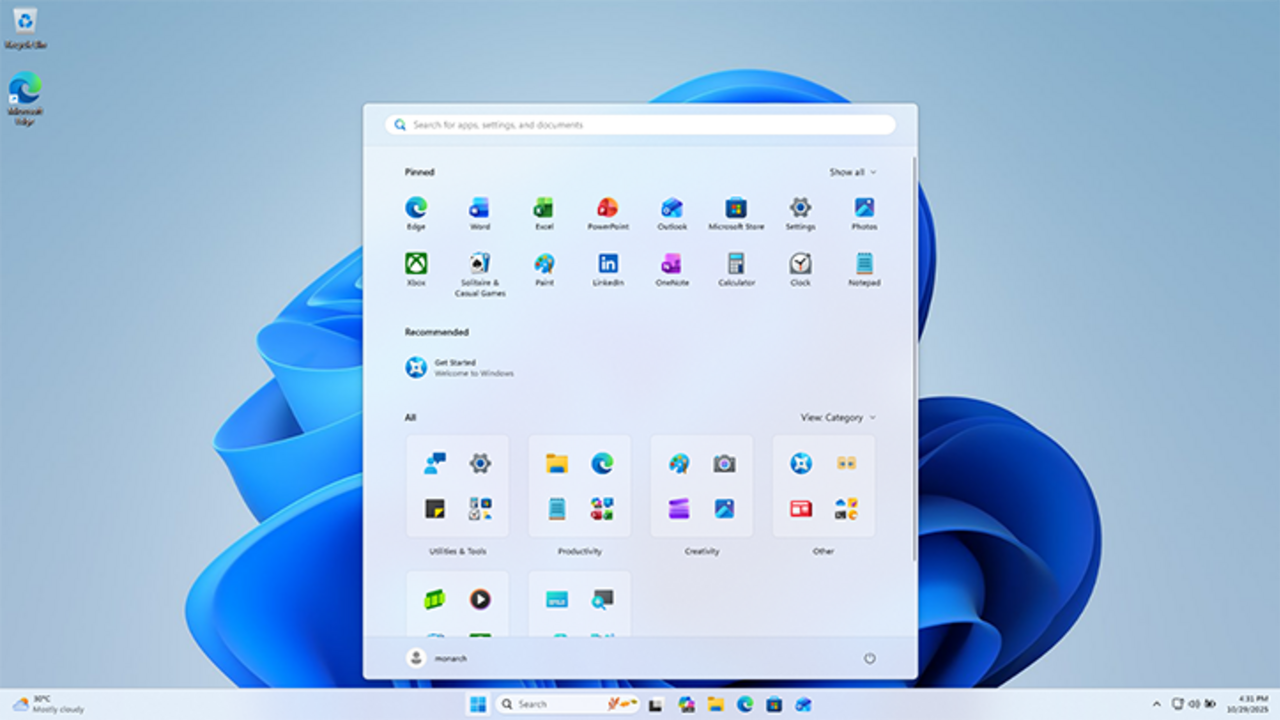 Captura real del escritorio de Windows 11 mostrando la barra de tareas centrada con el botón Inicio, íconos en el escritorio y el fondo Bloom característico.